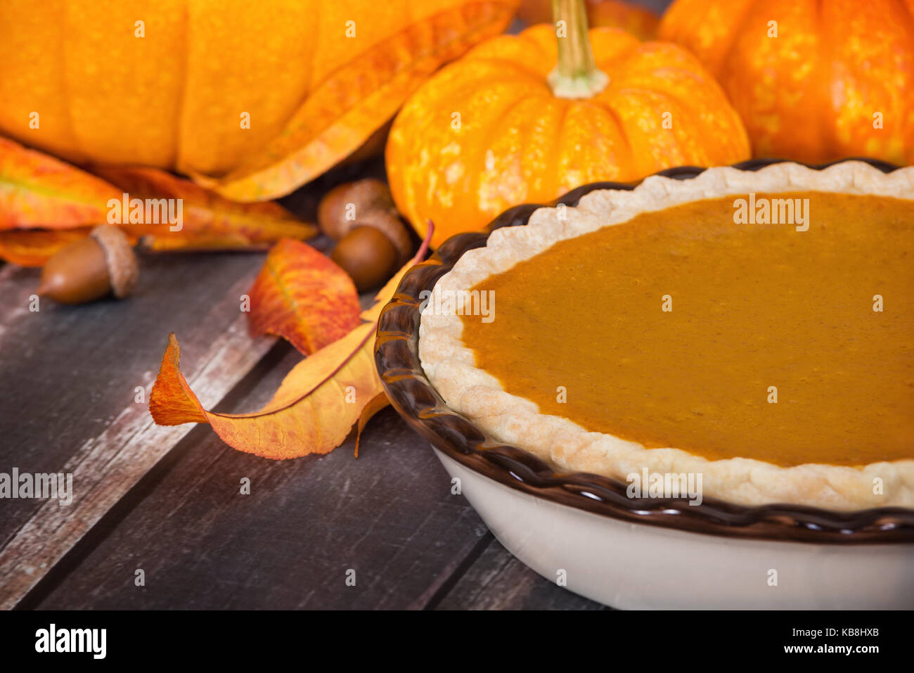 Pumpkin pie with pumpkins, golden autumn leaves, and acorns, on rustic table Stock Photo
