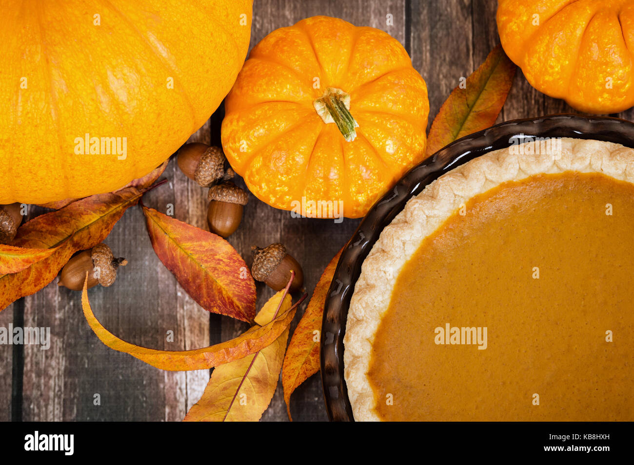 Pumpkin pie with pumpkins, autumn leaves, and acorns, on rustic table. Top view. Stock Photo