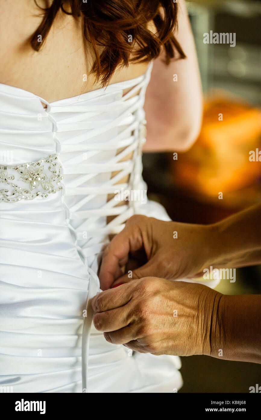 Mom is lacing up the back of her daughter's classy wedding dress. Stock Photo