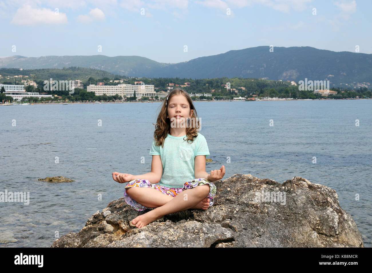 little girl sitting on a rock by the sea and meditates Stock Photo - Alamy