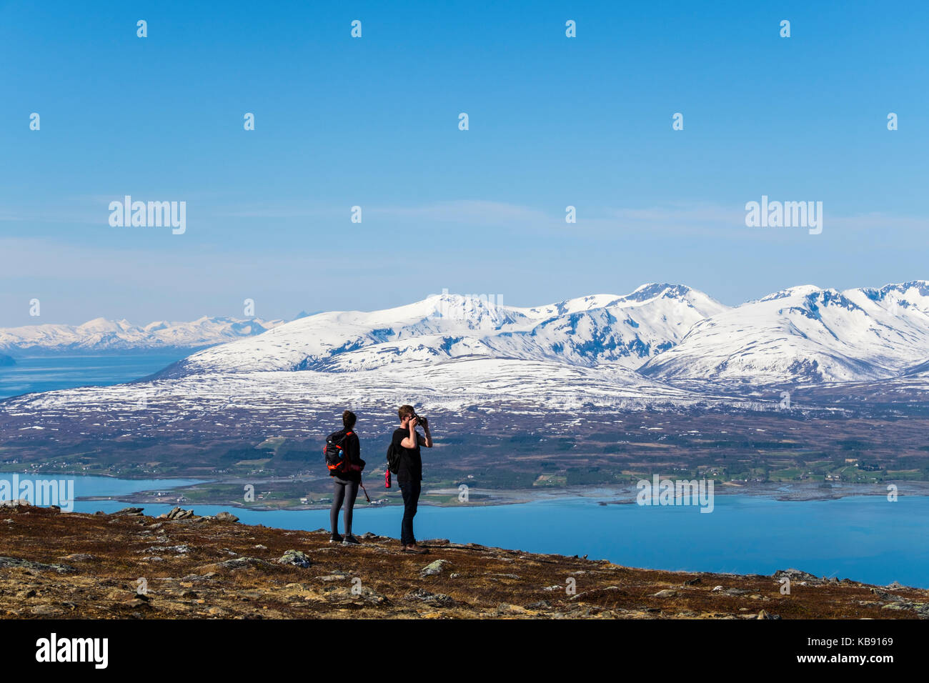 Hikers on Mount Storsteinen looking at scenic snowcapped mountains in summer. Tromso, Troms, Norway, Scandinavia Stock Photo
