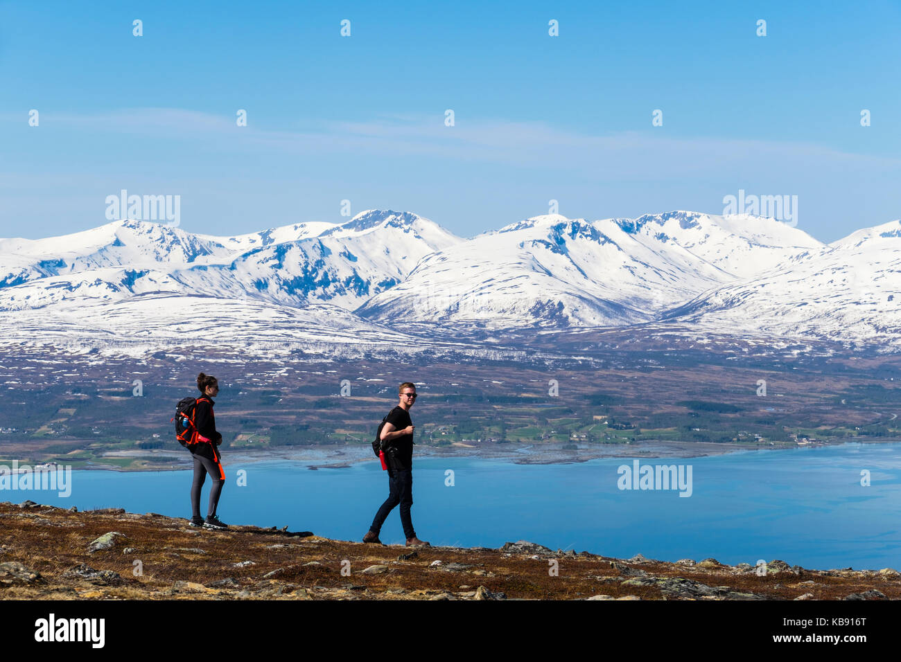 Hikers walking on Mount Storsteinen with backdrop of scenic snowcapped mountains in summer. Tromso, Troms, Norway, Scandinavia Stock Photo