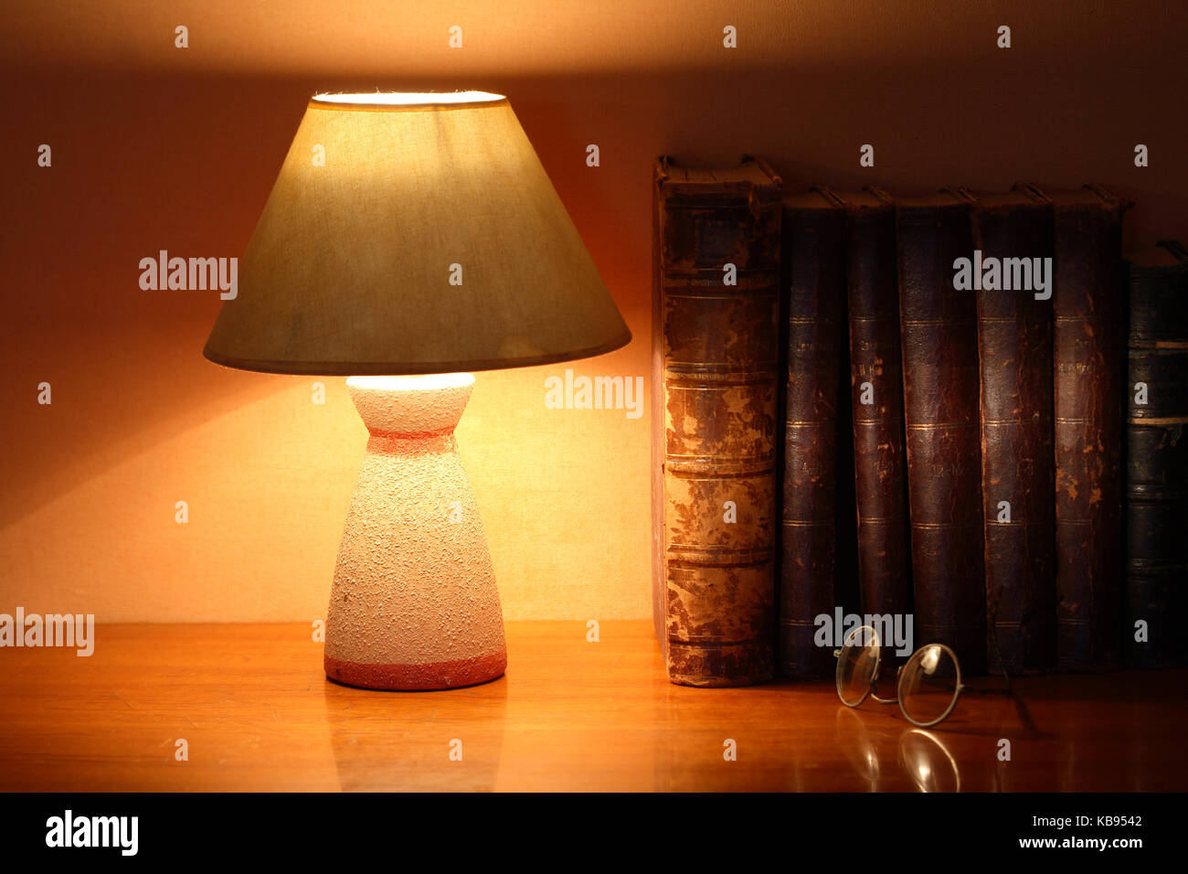 Luminous desk lamp near ancient books on ginger background with beam of