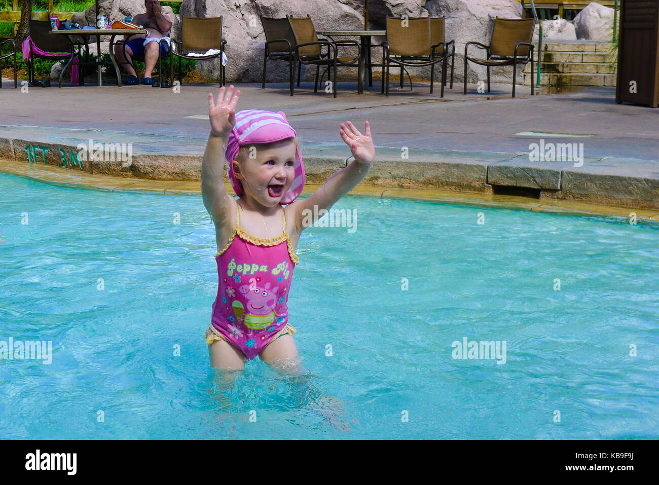 Child in a swim hat and peppa pig swimsuit standing in a swimming pool with  hands in the air in joy Stock Photo - Alamy