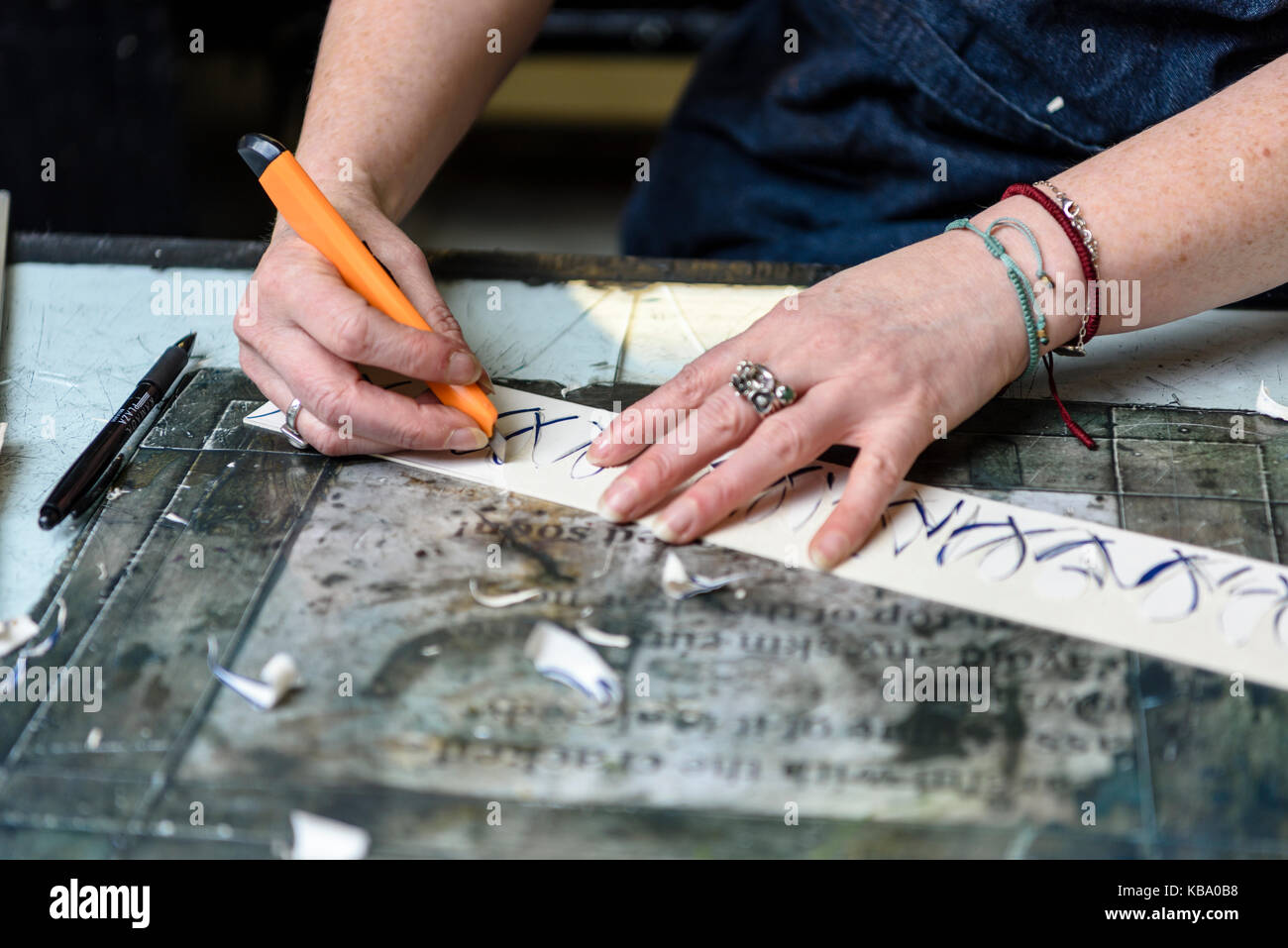 An artist uses a craft knife to cut a relief from a strip of linoleum