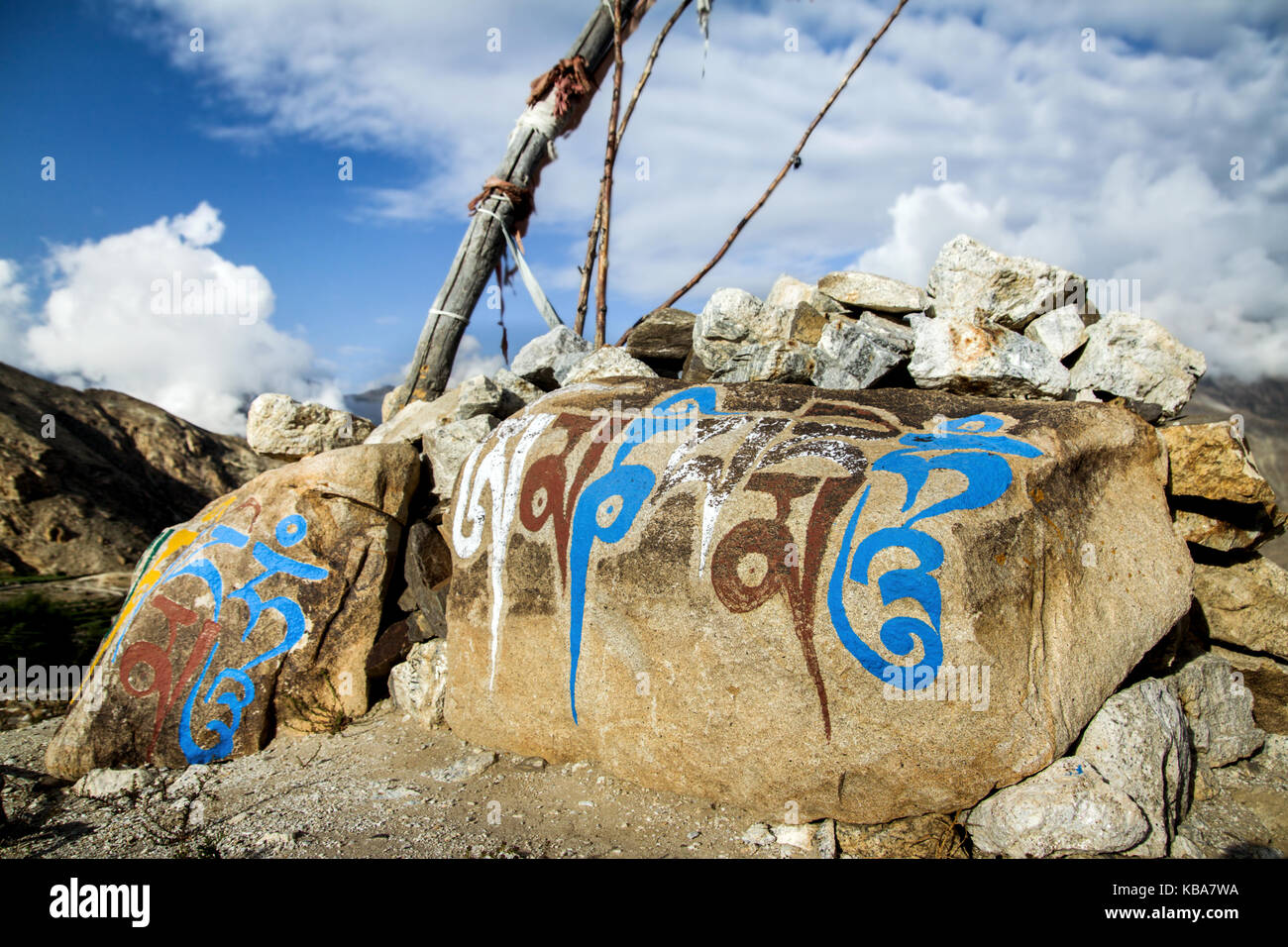 Om Mani Padme Hum sacred mantra of Buddhists painted on a rock in the Himalayan mountains of India. Sacred syllables of Tibetan Buddhism on blue sky Stock Photo