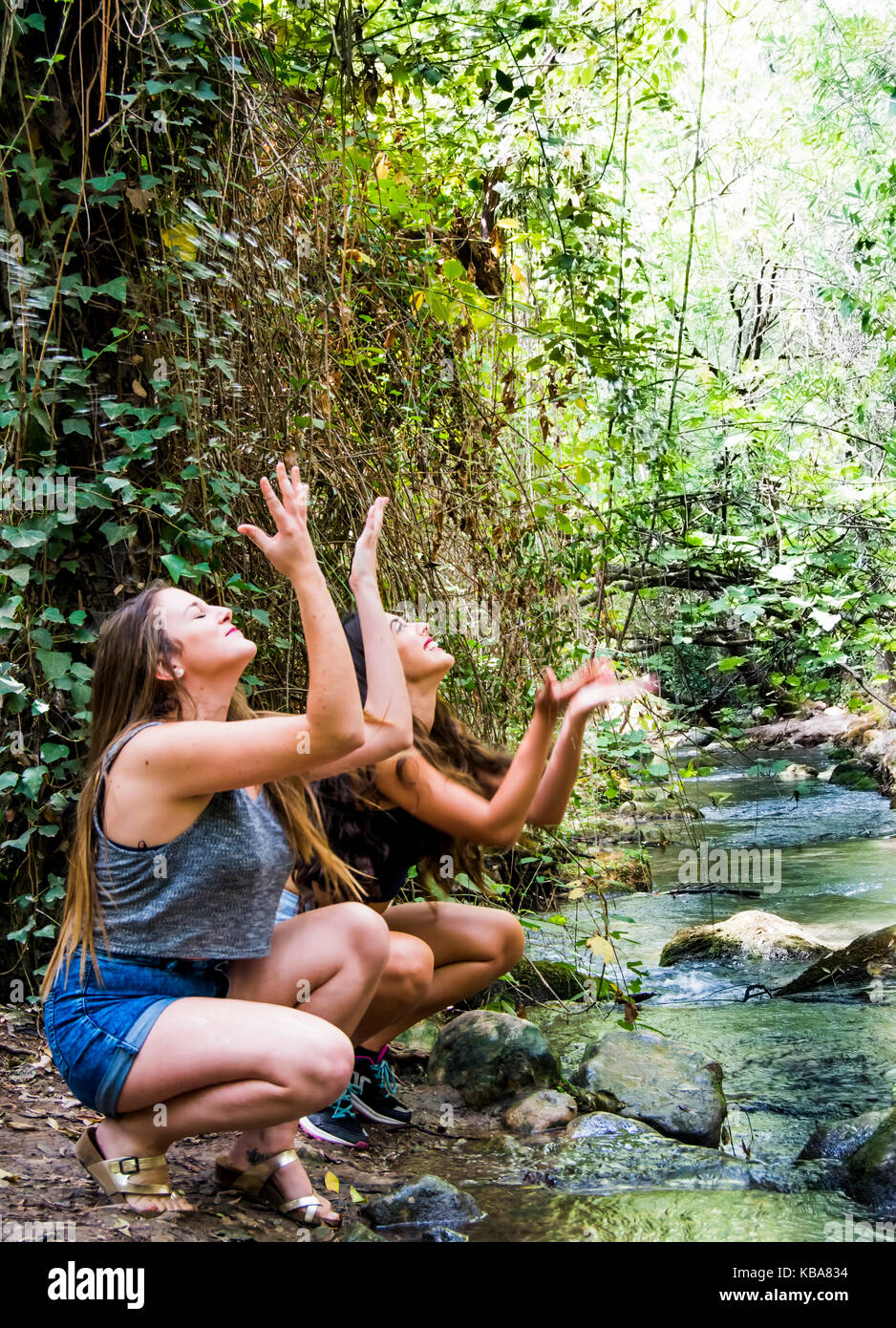 Two beautiful women in nature, splashing water in a river of a mountain ...