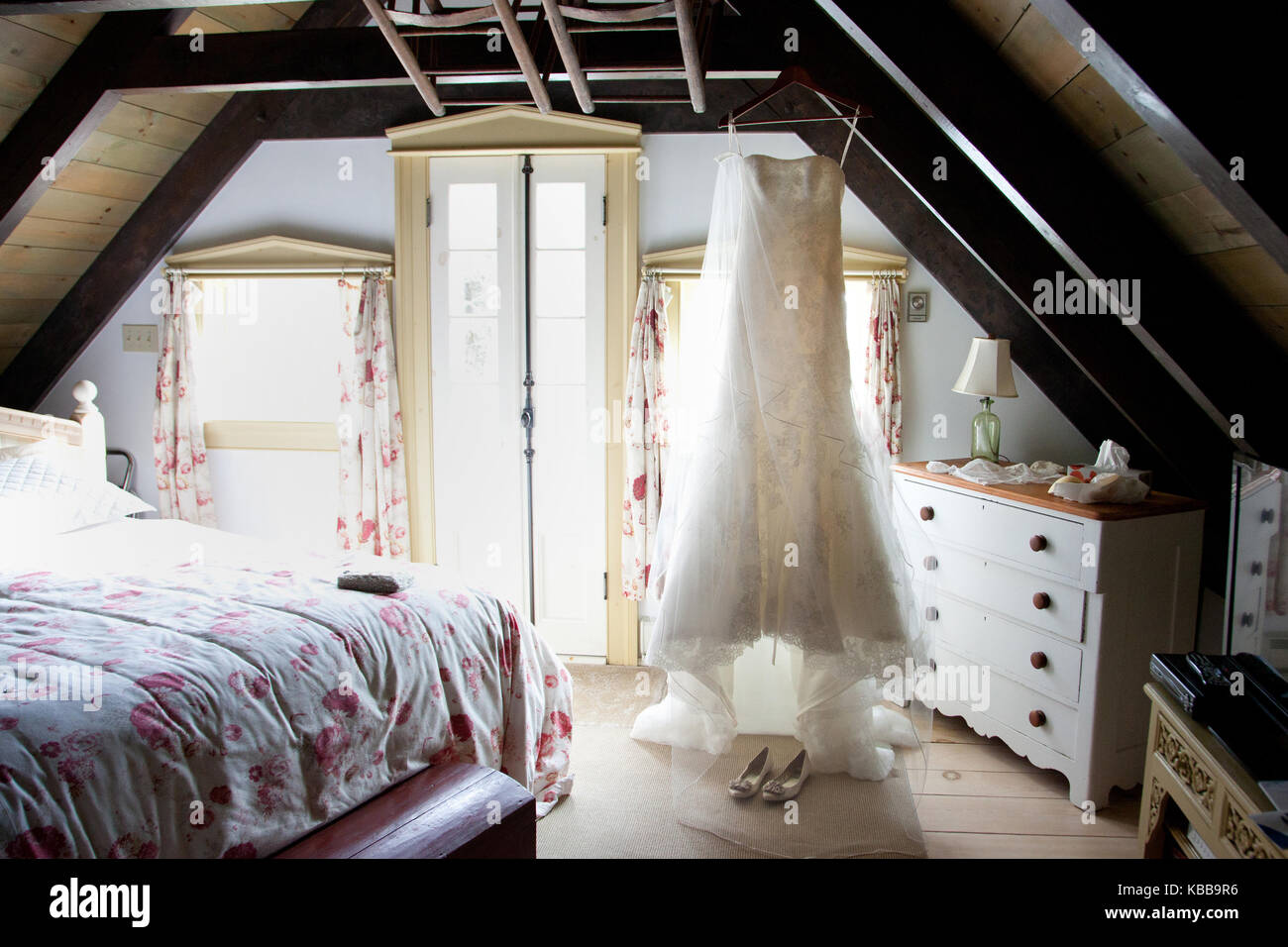 a white wedding gown hanging on a wooden beam ceiling in a rustic cabin Stock Photo