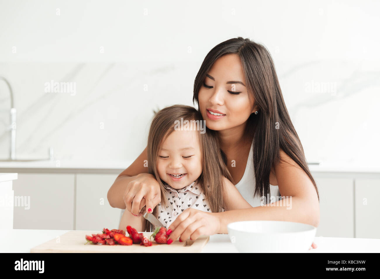 Smiling young asian woman cutting berries on a chopping board with her