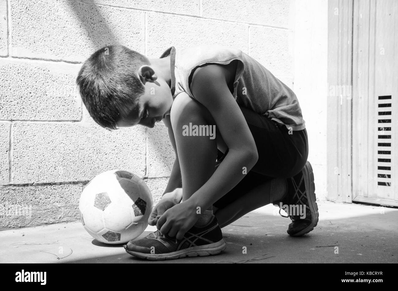 Street football. A young soccer player is wearing his shoes and is ready for a lonely training in the garage. Black and white image. Stock Photo
