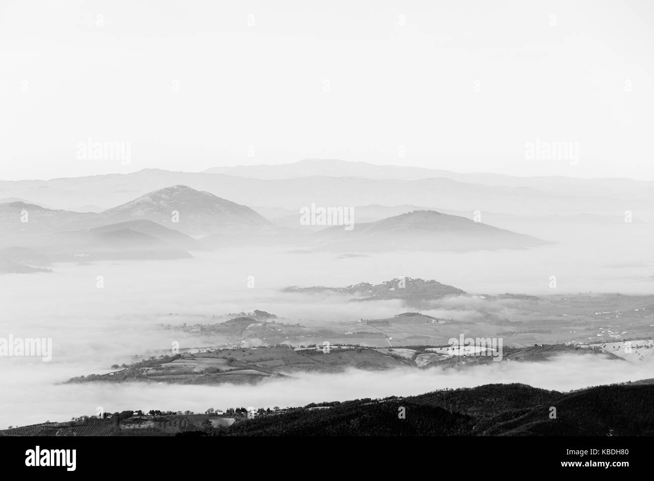 A valley filled by fog, with some hills in the foreground and other hills and mountains in the background Stock Photo