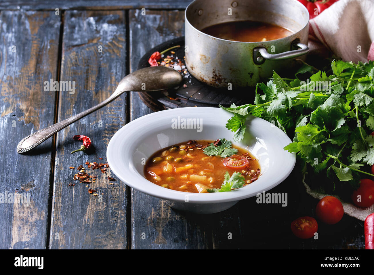 Vegetarian hot carrot tomato pea potato soup, served in plate and vintage aluminum pan with