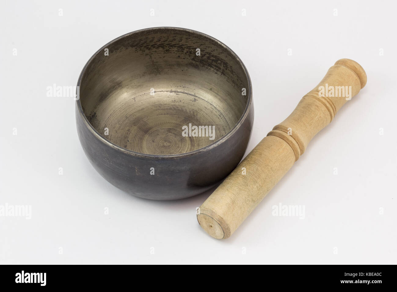 A singing bowl, made of metal, and a wooden stick lying next to it, on