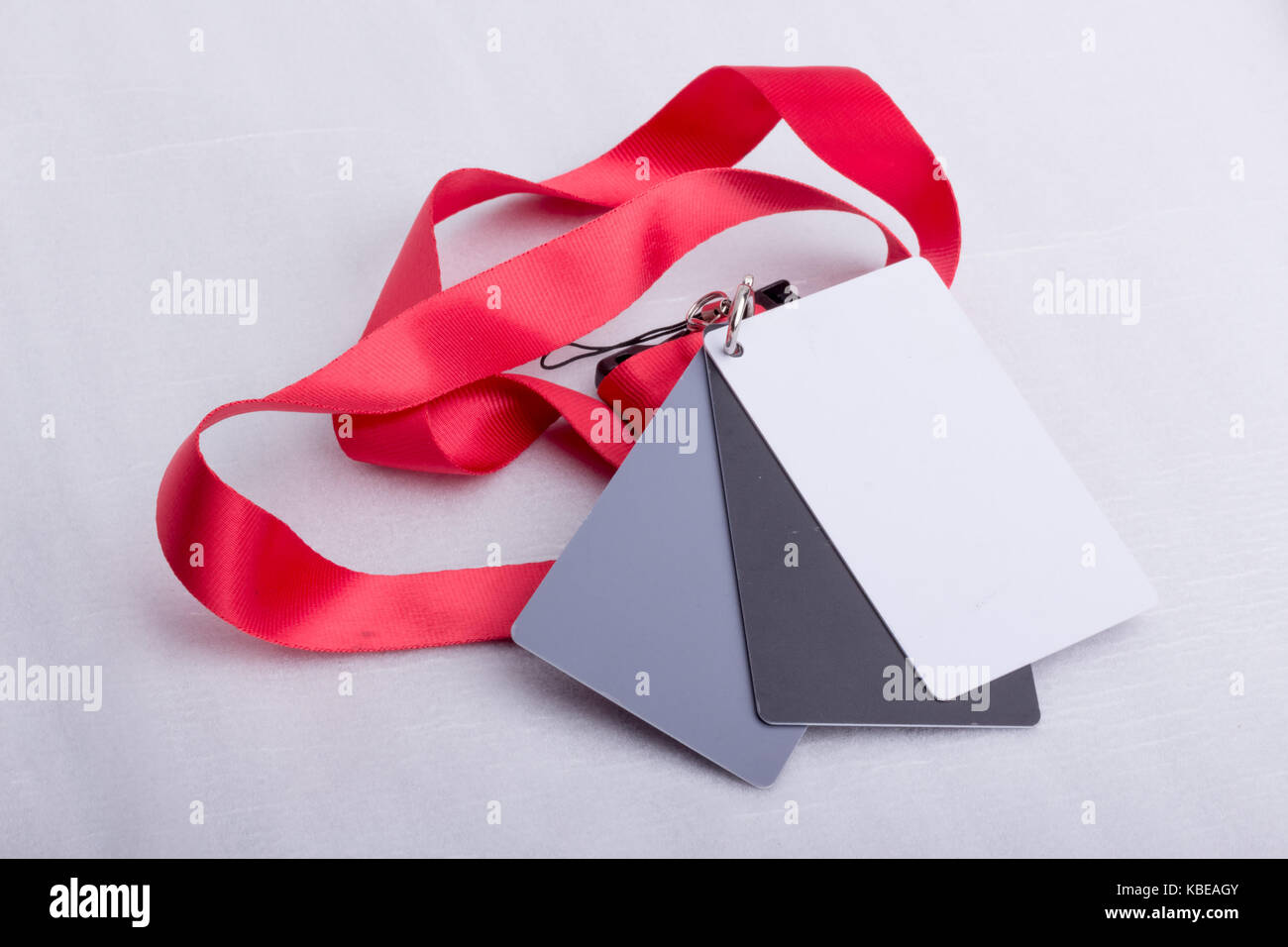 Three cards, one white, one grey and one black, attached together, and on a red strap, on a white surface. Stock Photo