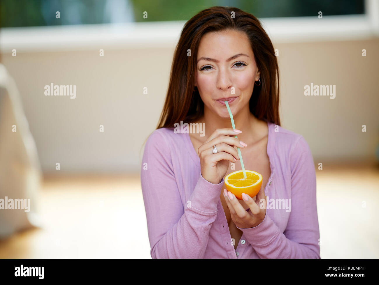 Girl sat holding orange and a straw Stock Photo