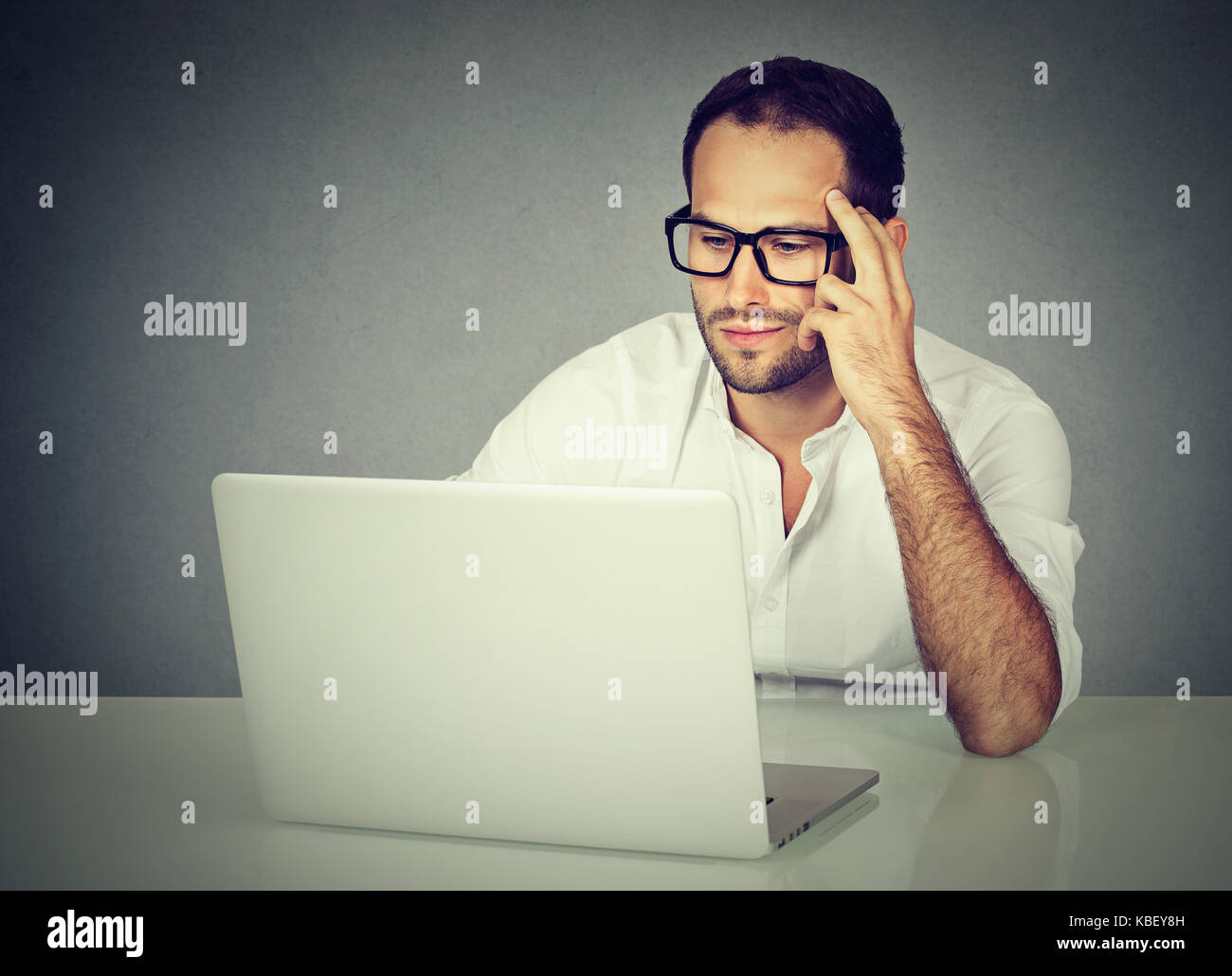 Closeup of a pensive businessman wearing glasses sitting at desk working on his laptop Stock Photo