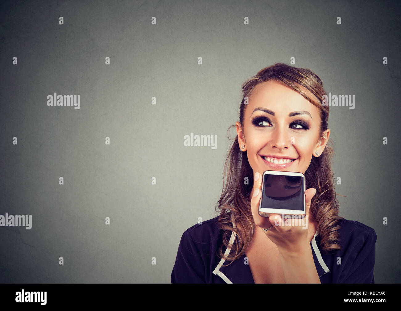 Girl using a smart phone voice recognition function online on gray wall background Stock Photo