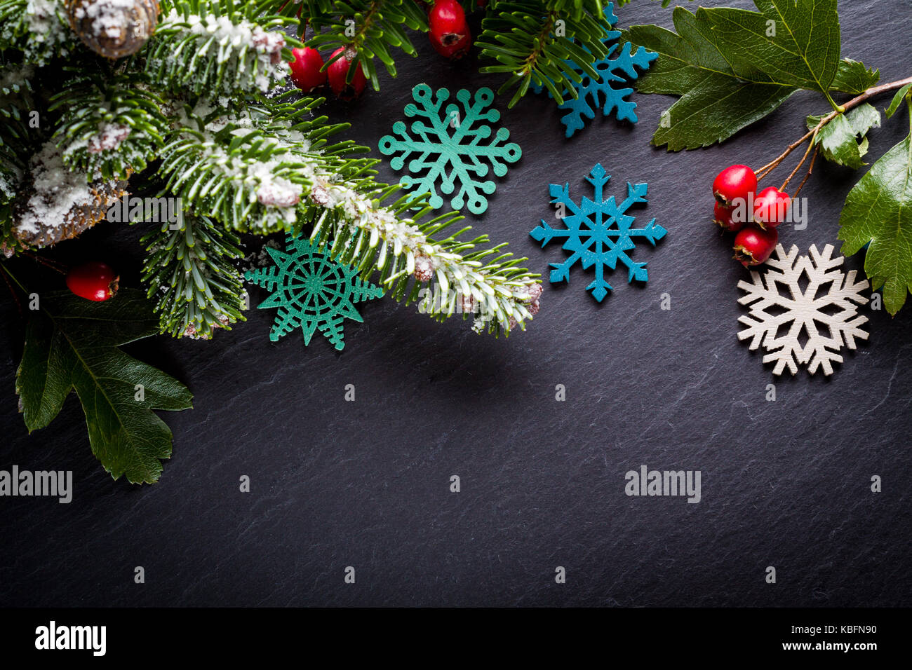 Background christmas decoration twig, red berries and wooden stars on back slate. Stock Photo