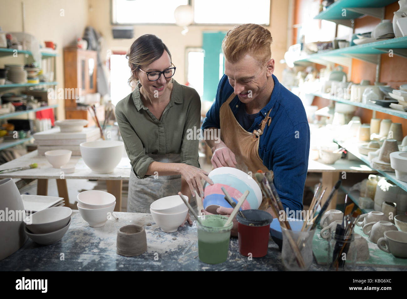 Male and female potter interacting with each other in pottery workshop ...