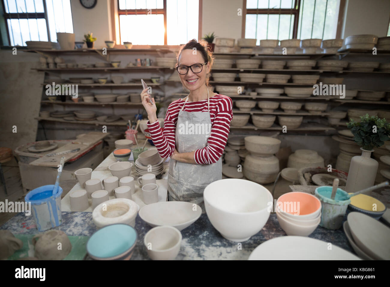 Portrait of female potter standing with mobile phone in pottery ...