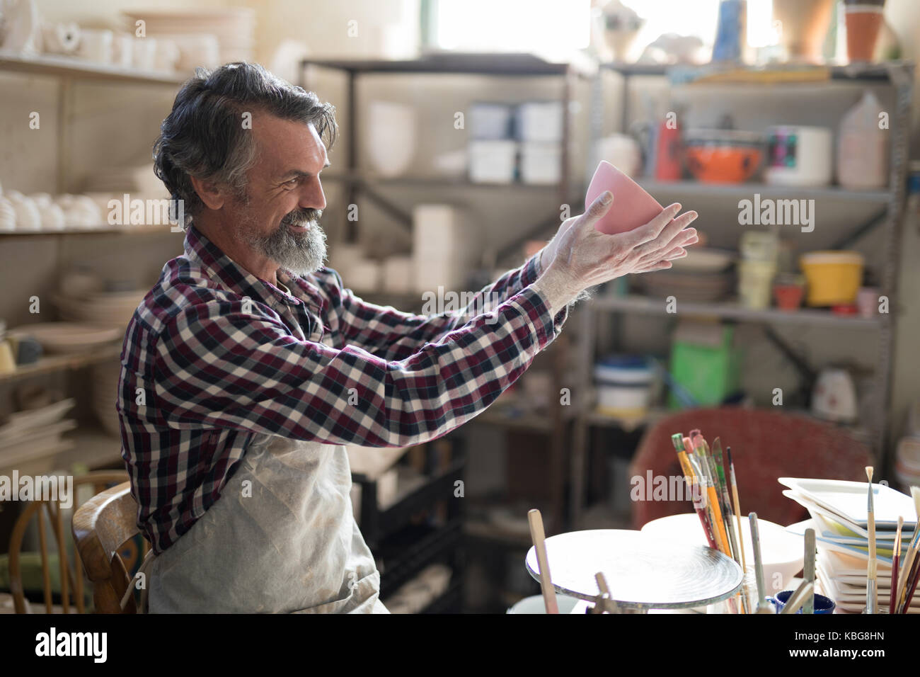 Male potter looking at painted bowl in pottery workshop Stock Photo - Alamy