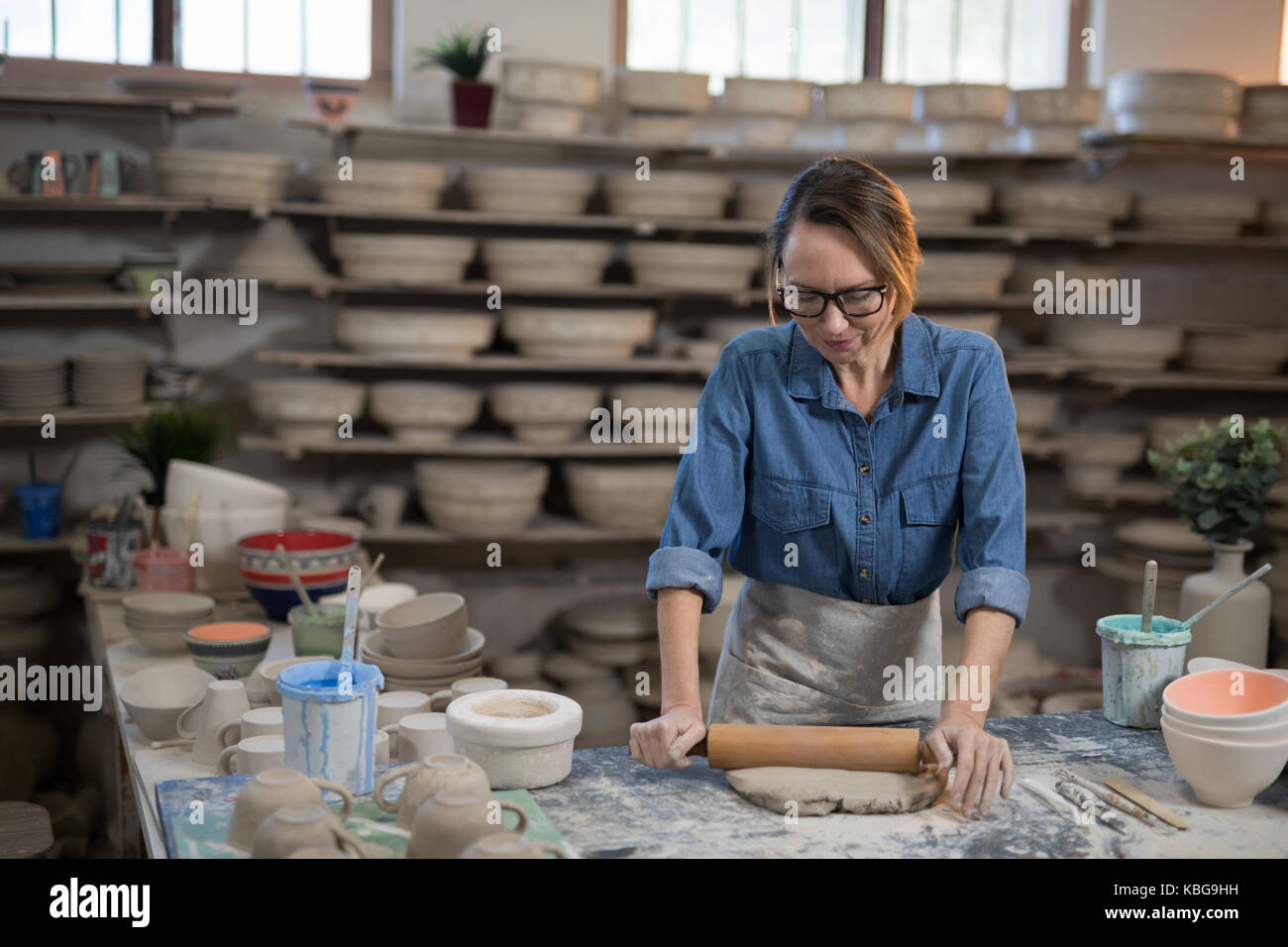 Female potter flattening the clay with rolling pin in workshop Stock Photo