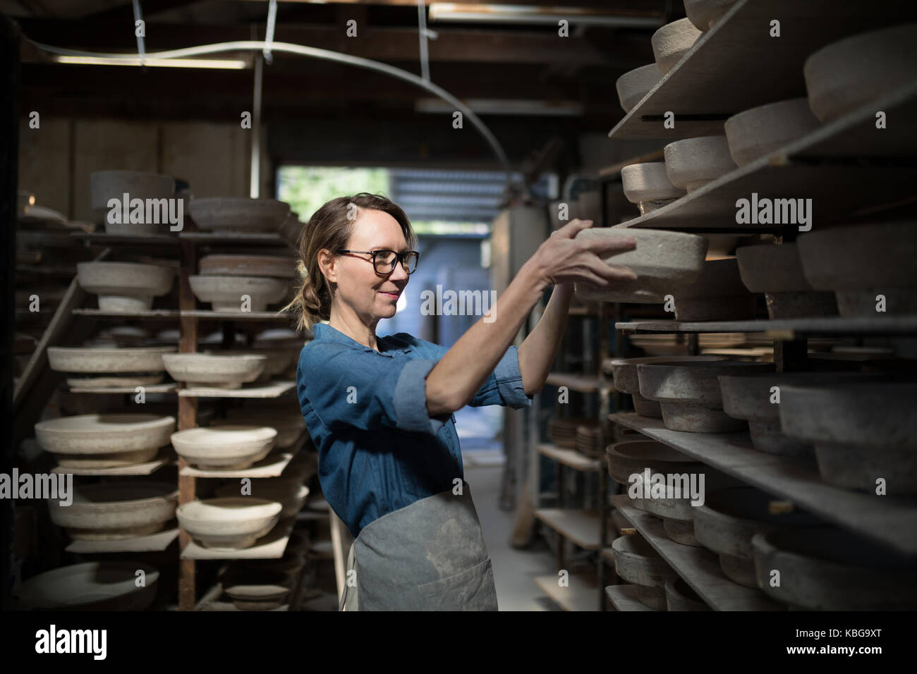 Female potter placing bowl in shelf at pottery workshop Stock Photo - Alamy
