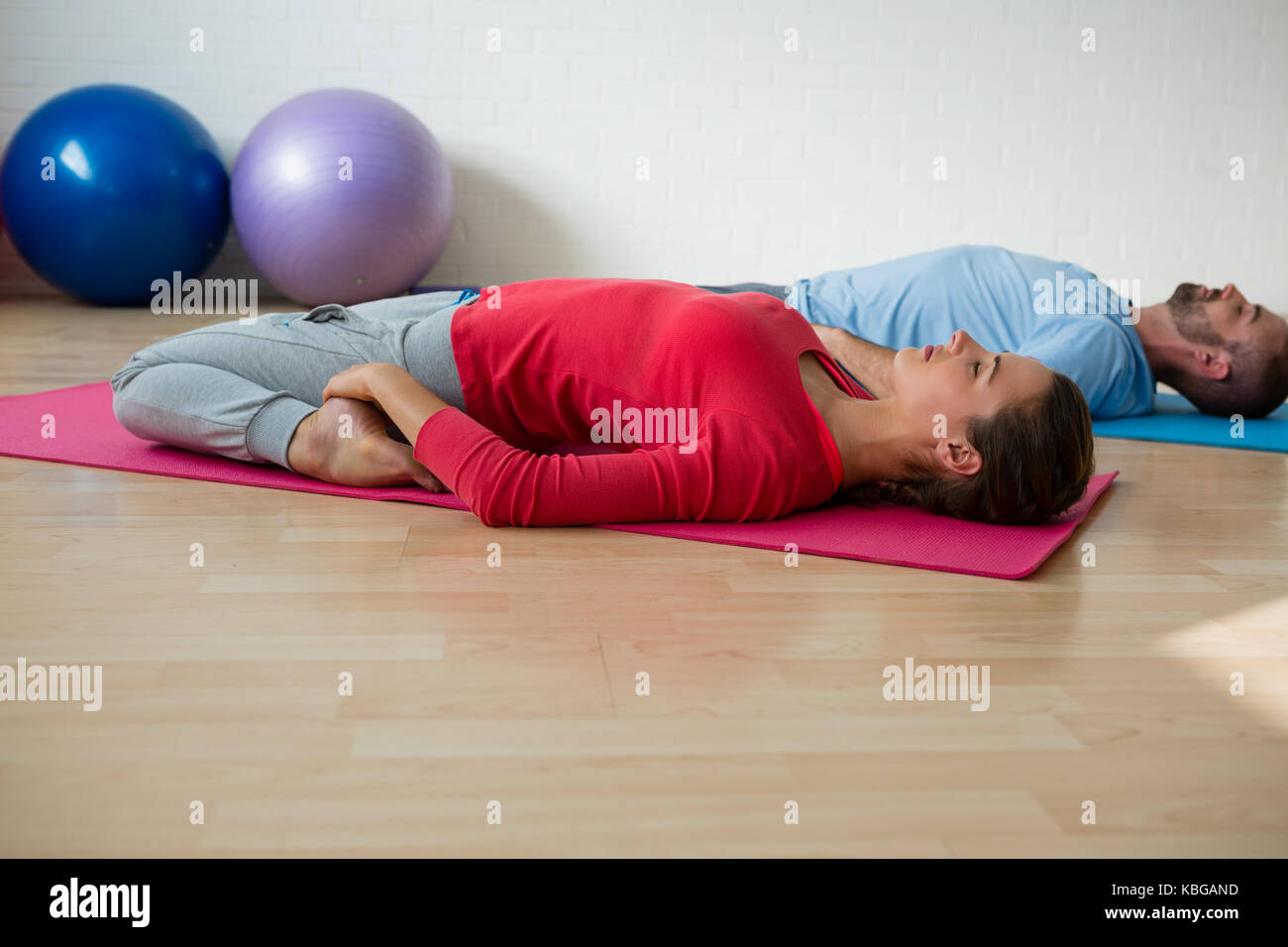 Instructor with student practicing reclined hero pose in yoga studio Stock Photo