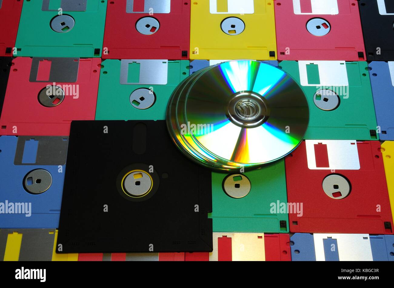 Old diskette 5 25 inches with 3.5 floppy disks of various colors with modern DVD. Background Stock Photo