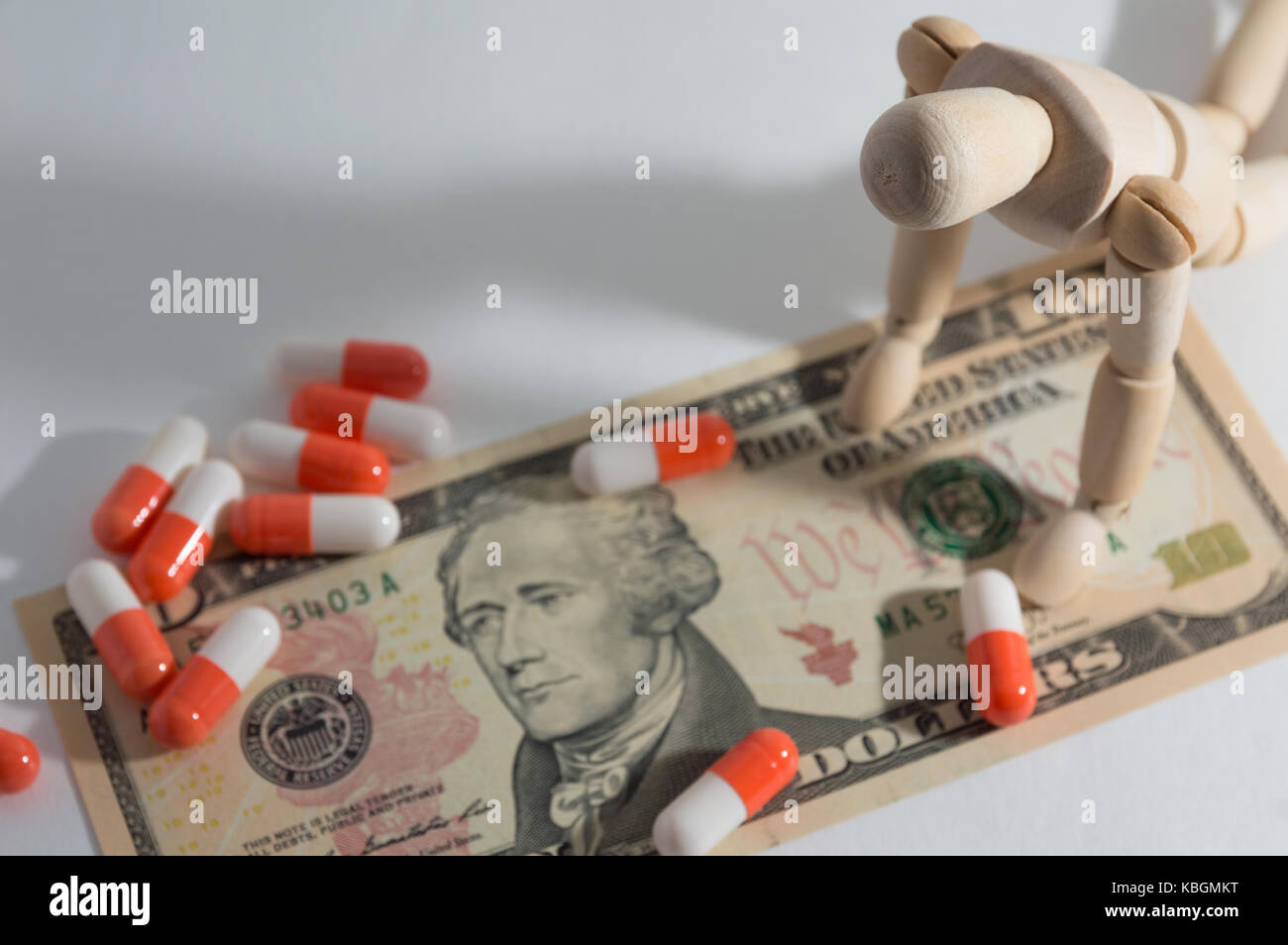 Wooden jointed doll kneeling down and pill on dollar Stock Photo