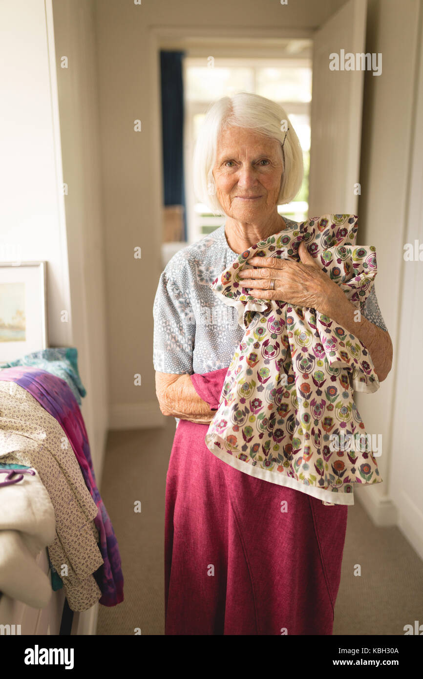 Portrait of senior woman holding clothes at home Stock Photo