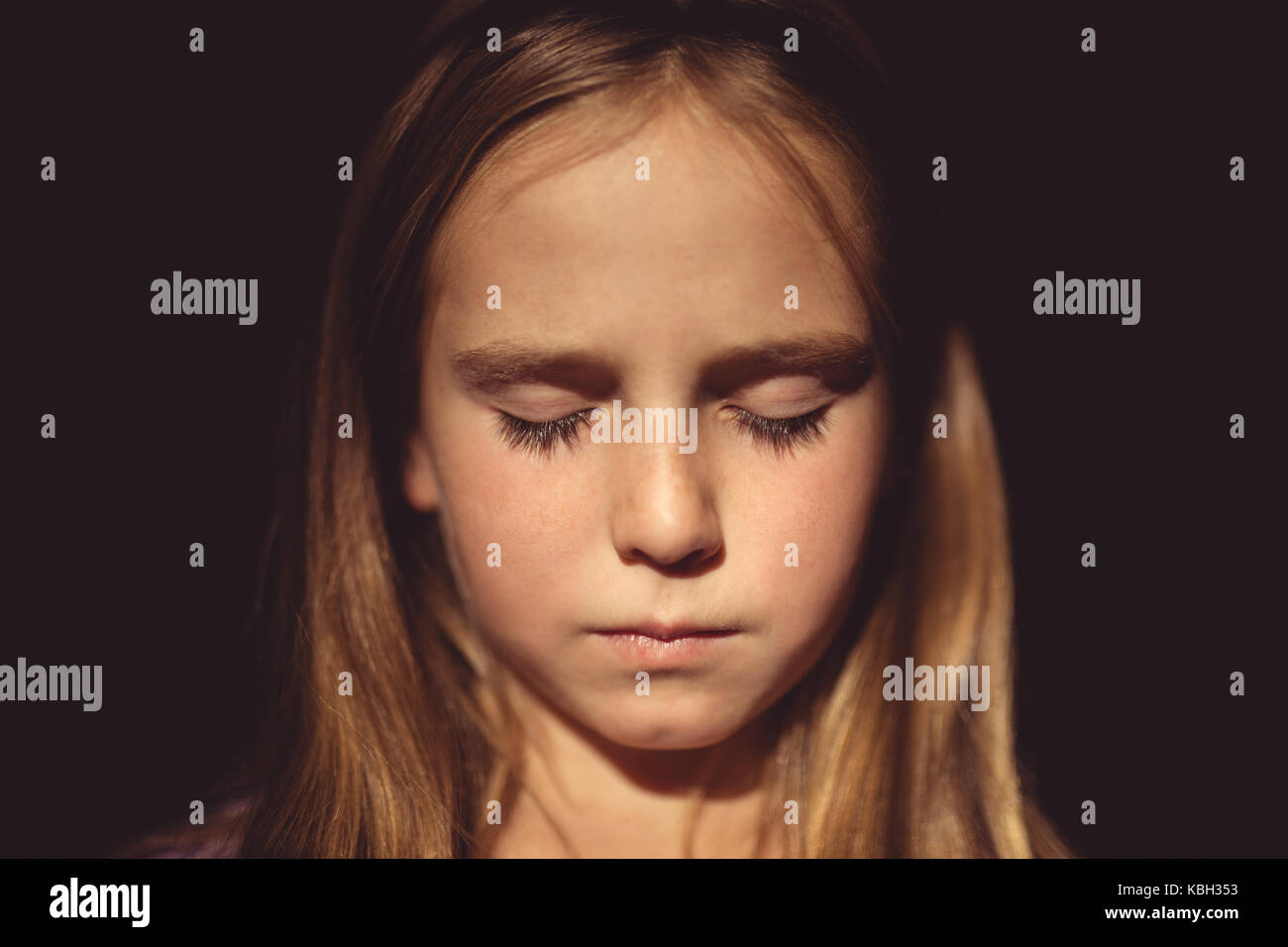 Girl with eyes closed against black background Stock Photo