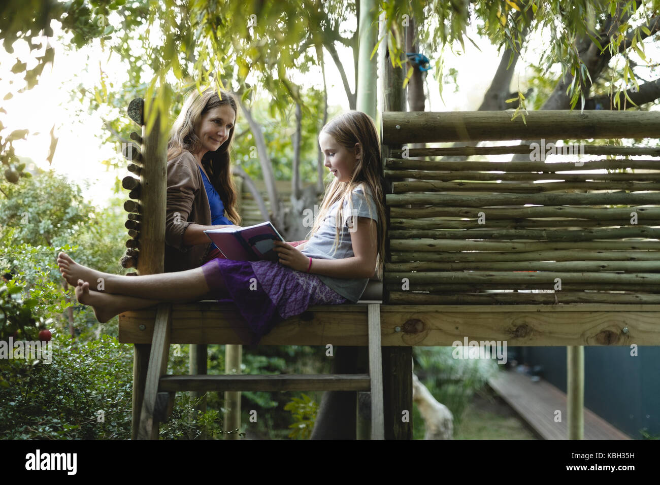 Smiling granddaughter and grandmother reading book on a tree house on a sunny day Stock Photo