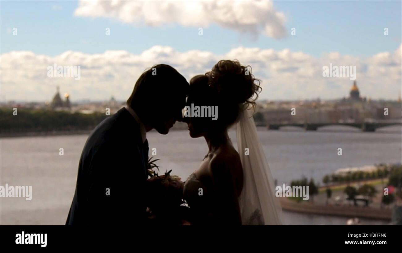 Bride and groom stand smiling in a front of a window hidden by golden ...
