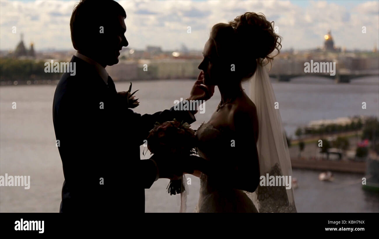 Bride and groom stand smiling in a front of a window hidden by golden ...