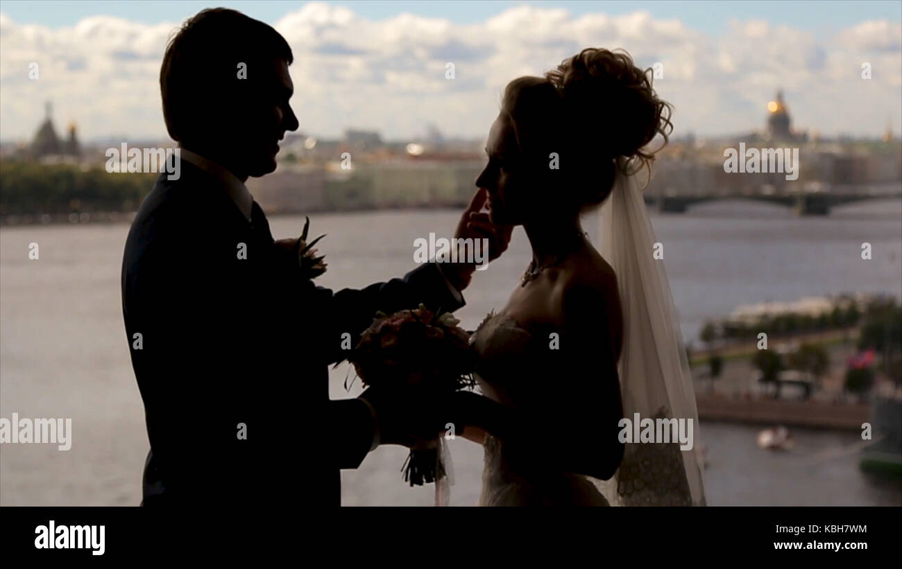 Bride and groom stand smiling in a front of a window hidden by golden ...