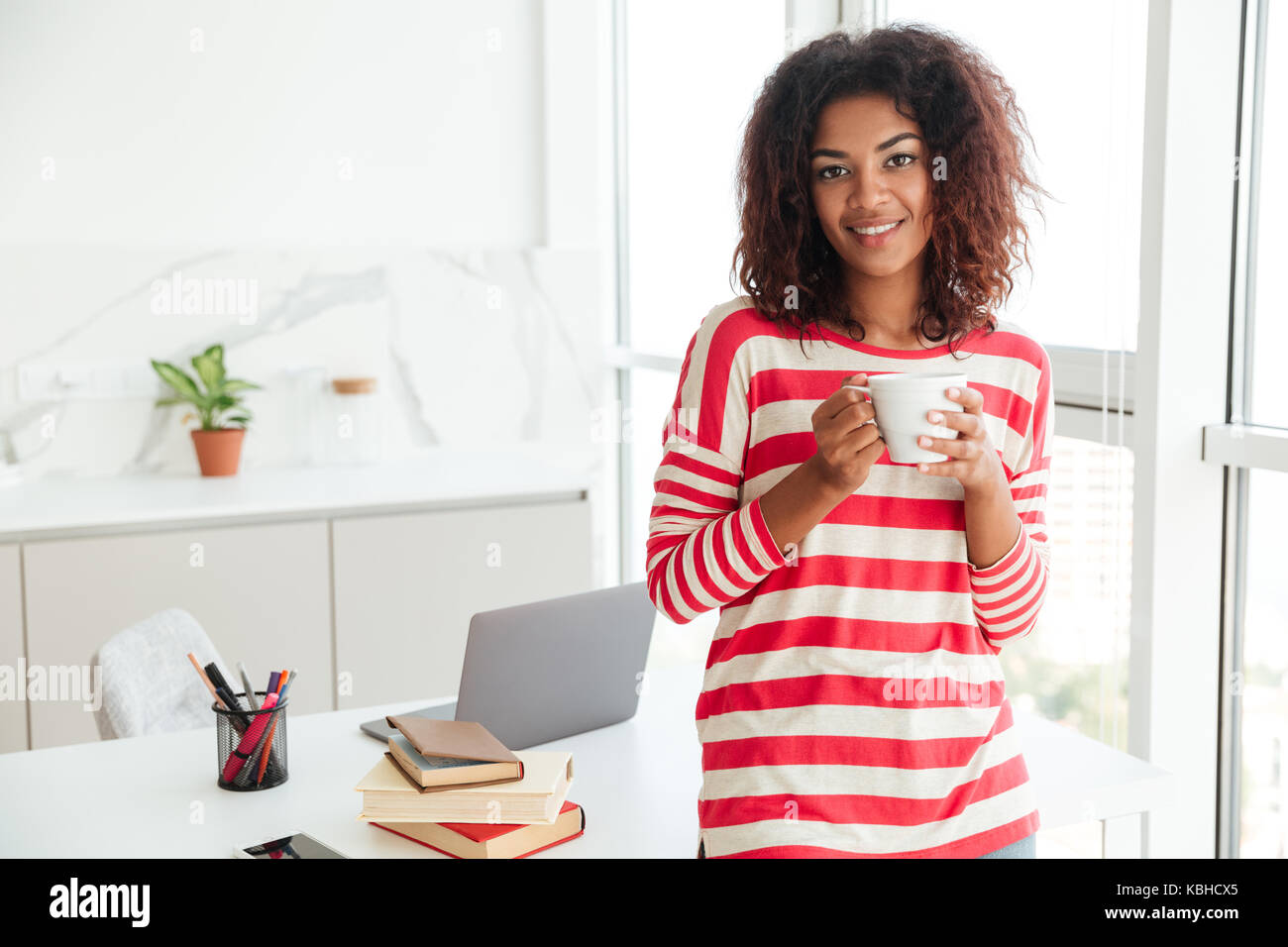 Smiling african woman drinking coffee and looking at the camera while ...