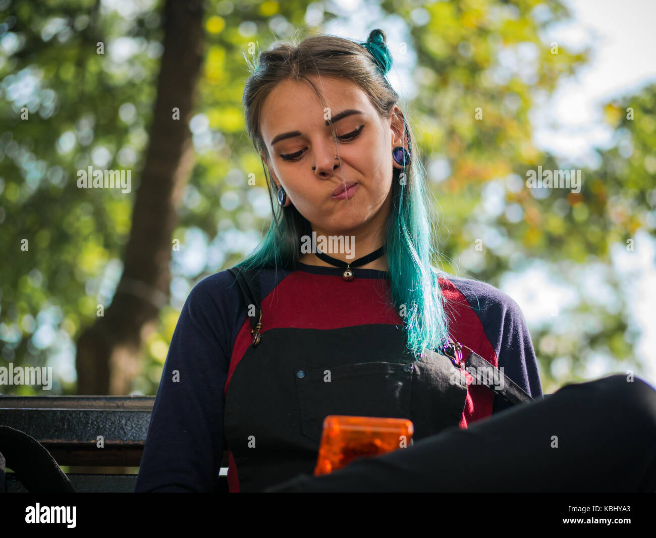 hipster girl playing tetris game in European park. Portrait of teen girl with blue dyed hair,piercing in nose,violet lenses and unusual hairstyle.Old  Stock Photo