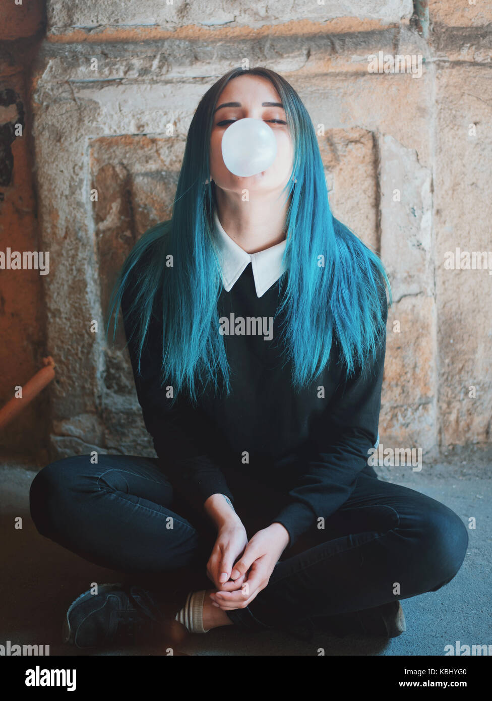 Cute gothic model blows bubblegum. Street punk or hipster woman student with blue colorful dyed hair, piercing,lenses,ears tunnels and unusual hairsty Stock Photo