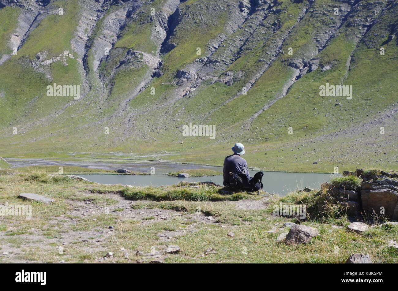 A sitting man admires a mountain landscape with lake and summit Stock Photo