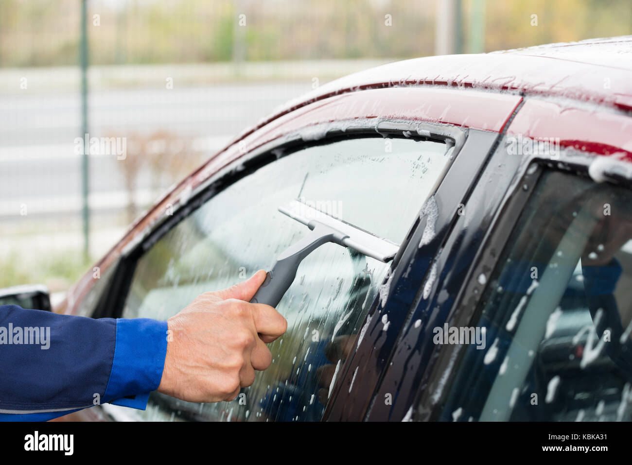Cropped image of serviceman cleaning car window with wiper at service station Stock Photo