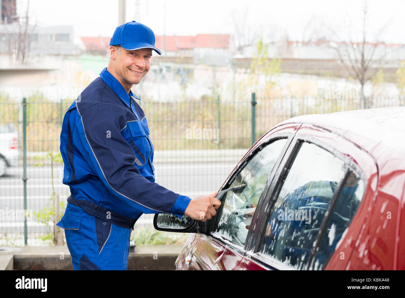 Mature serviceman cleaning car window with wiper at service station Stock Photo