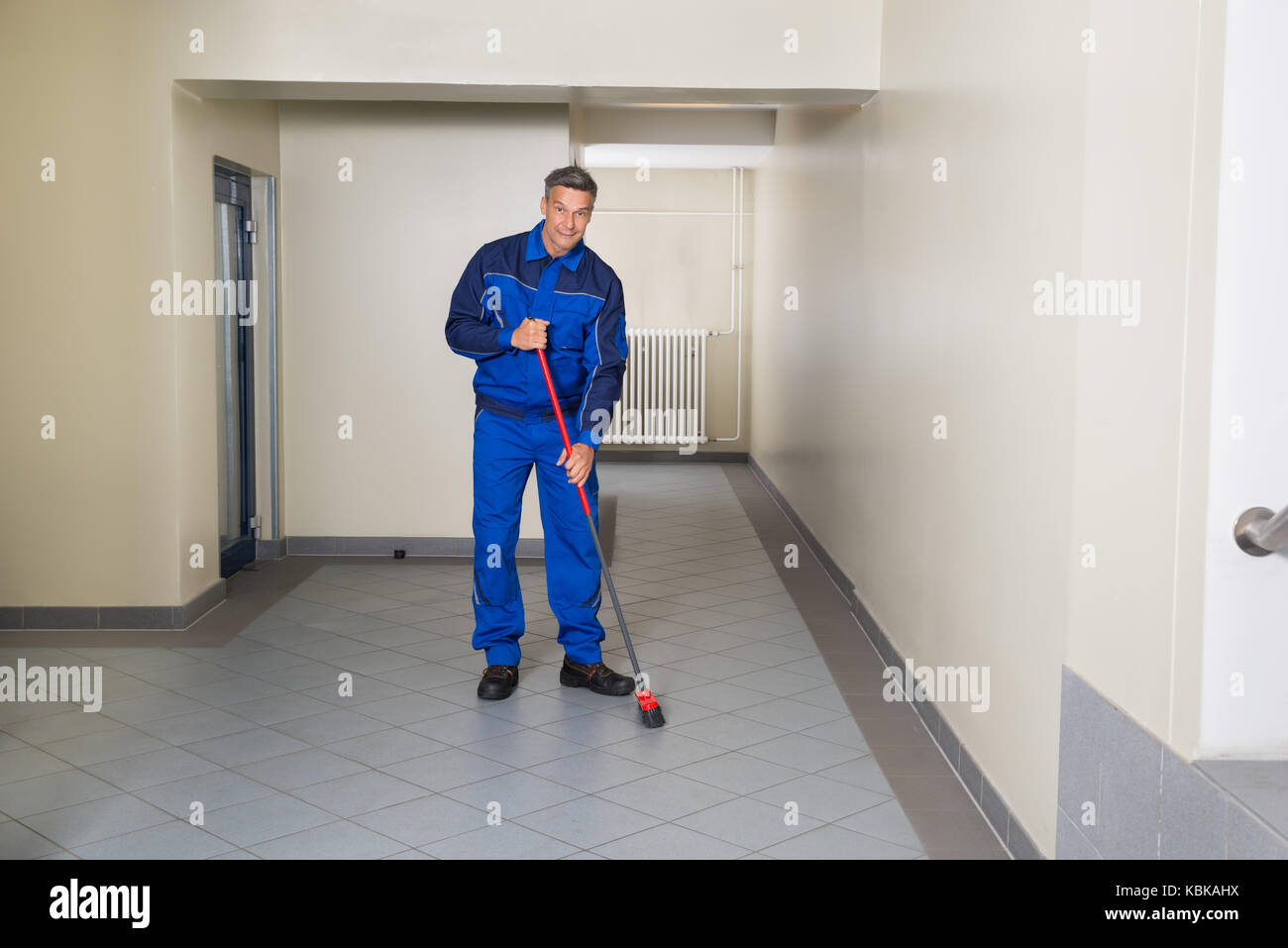 Full length of mature male worker with broom cleaning office corridor Stock Photo