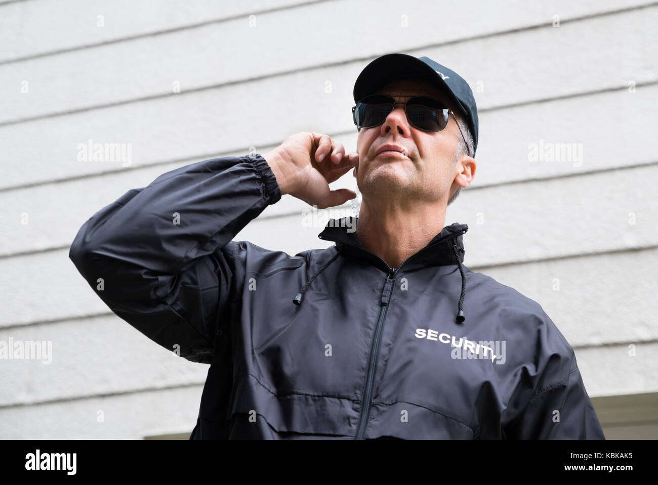 Confident mature security guard listening to earpiece against building Stock Photo