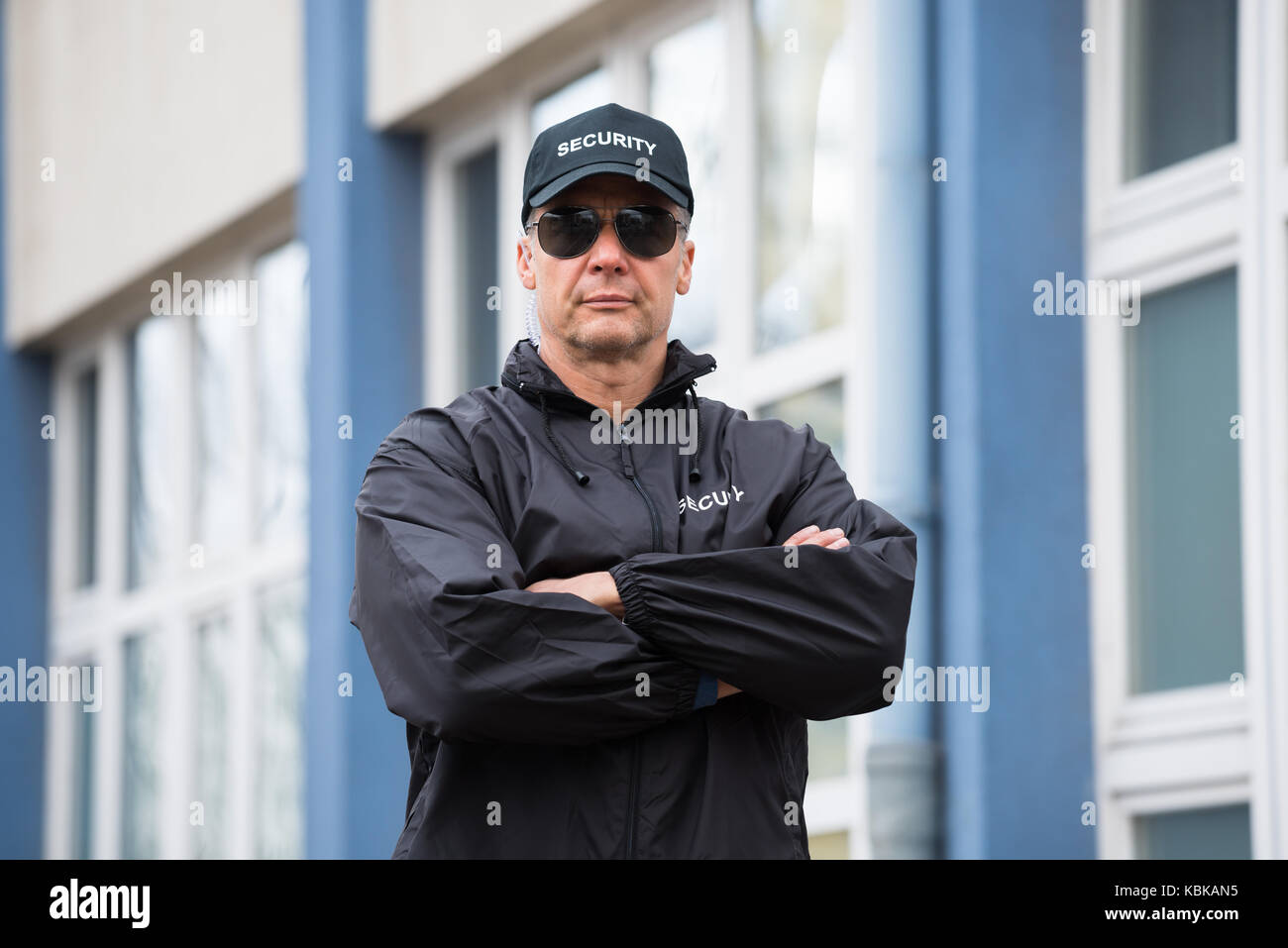 Portrait of confident mature security guard standing arms crossed outside building Stock Photo