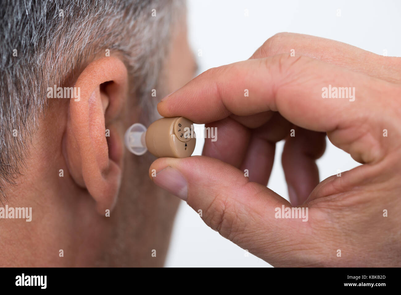 Closeup of businessman inserting hearing aid in ear over white ...