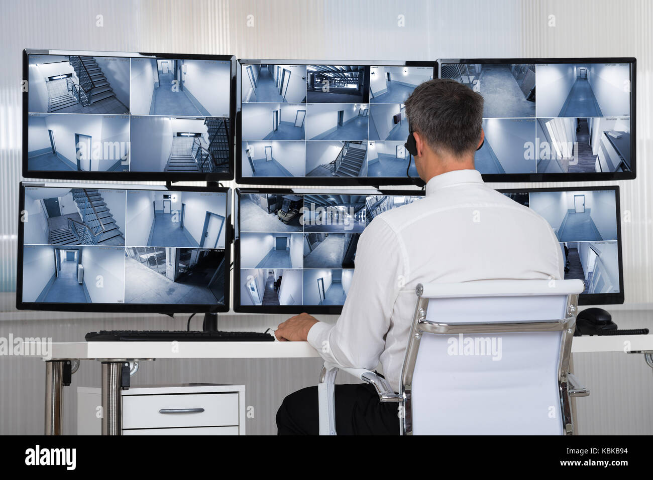 Rear view of security system operator looking at CCTV footage at desk