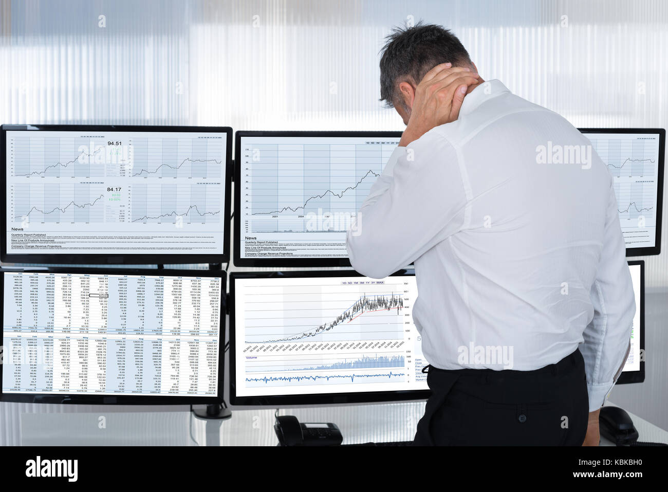 Rear view of stock market broker suffering from neck pain by multiple screens in office Stock Photo