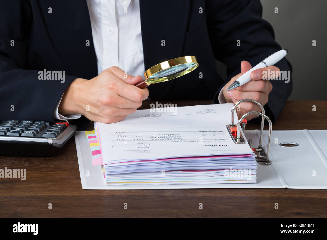 Midsection of young businesswoman scrutinizing bills with magnifying glass at desk Stock Photo