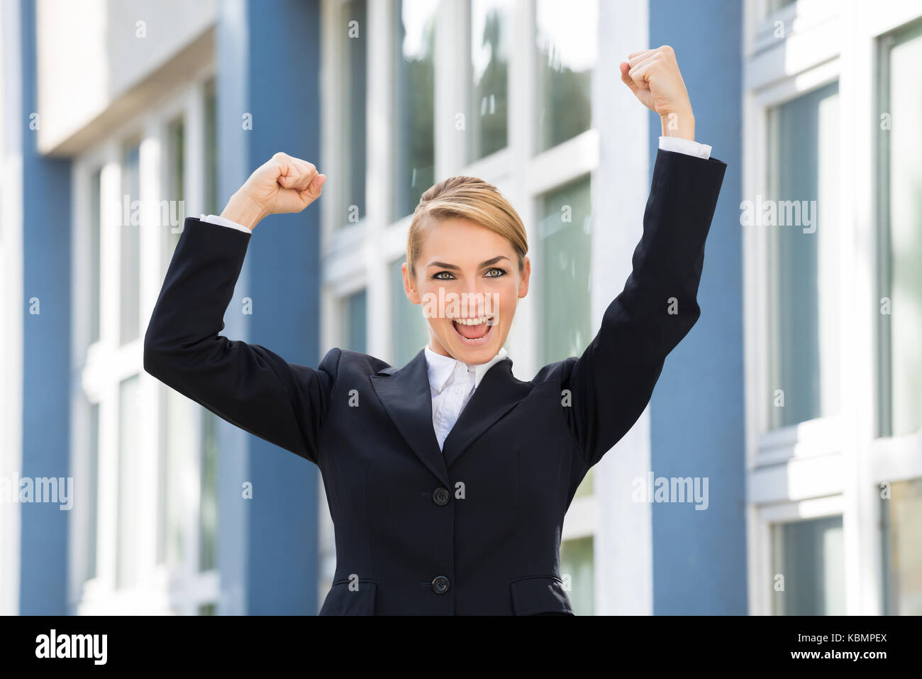 Happy businesswoman raising arms to celebrate success with building in background Stock Photo